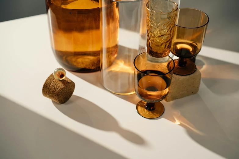 a couple of glasses sitting on top of a table, a still life, inspired by Joseph Beuys, unsplash, new objectivity, glowing amber, birch, textured base ; product photos, various sizes