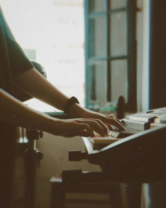 a person playing a keyboard in front of a window, an album cover, trending on pexels, lgbtq, muted tones, coherent hands, sitting on a mocha-colored table