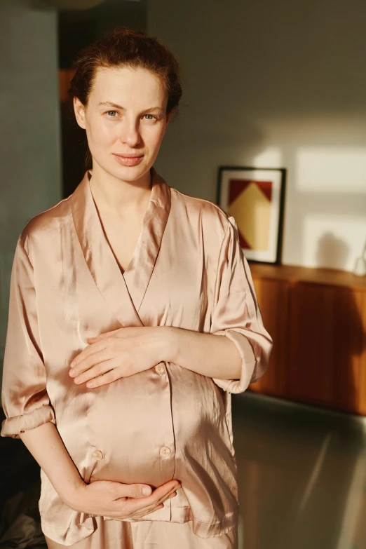 a woman standing in a room with her hands on her stomach, an album cover, by Nina Hamnett, reddit, renaissance, pale pink and gold kimono, maternity feeling, a full portrait of nordic female, close - up portrait shot