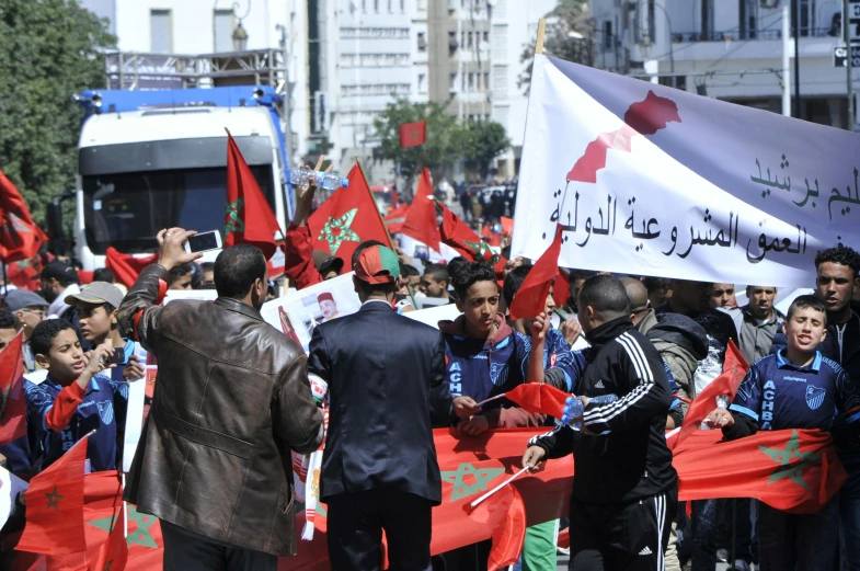 a large group of people holding red and white flags, pexels, hurufiyya, moroccan city, protesters holding placards, 🚿🗝📝, flowers around