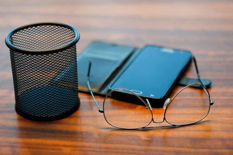 a pair of glasses and a cell phone on a table, trending on pexels, mesh wire, round black glasses, sitting on a desk, sustainable materials