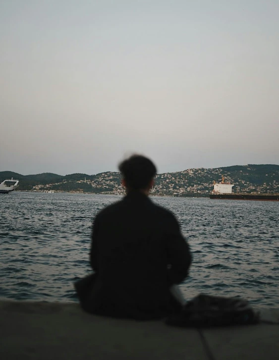 a person sitting in front of a body of water, waiting