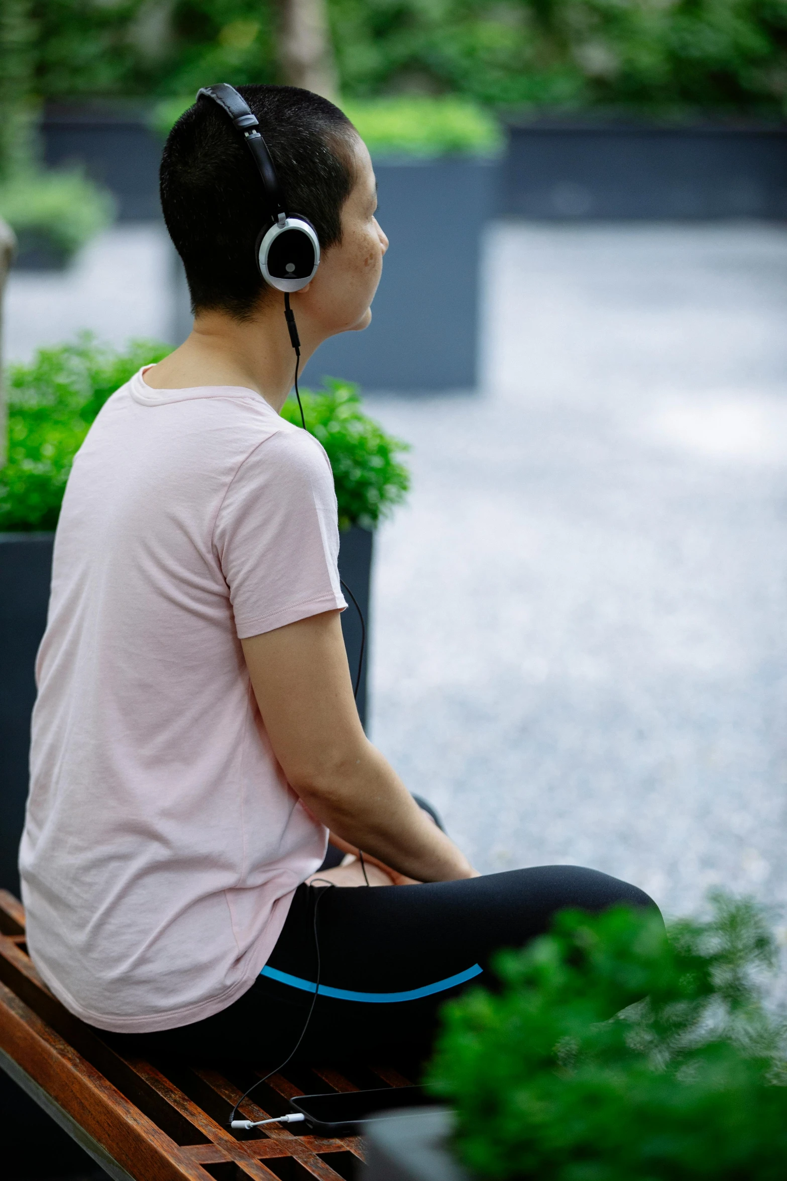 a woman sitting on a bench wearing headphones, happening, from the distance, headspace, circular, next to a plant
