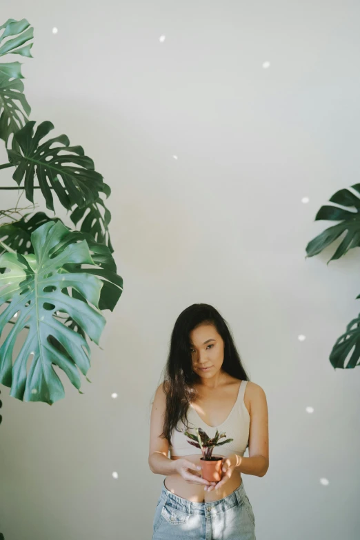 a woman holding a potted plant in her hands, inspired by Ren Hang, unsplash, minimalism, wearing a crop top, tropical lighting, with crystals on the walls, an asian woman