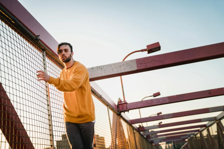 a man riding a skateboard across a bridge, a portrait, by Niko Henrichon, pexels contest winner, long orange sweatshirt, yellow, pose, sam nassour