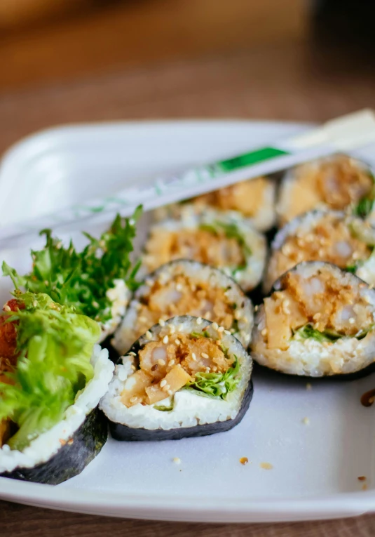 a white plate topped with sushi on top of a wooden table, 6 pack, square, adi meyers, close - up photograph