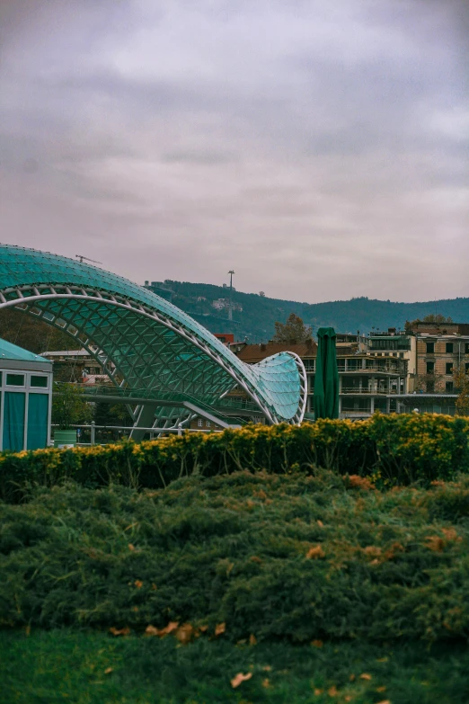 a statue of a fish sitting on top of a lush green field, tall bridge with city on top, rounded roof, italy, biodome