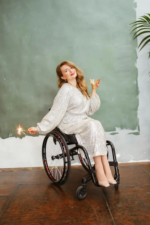 a woman in a wheelchair holding a lit candle, by Zofia Stryjenska, trending on pexels, wearing silver dress, casual pose, having fun, glitter dress