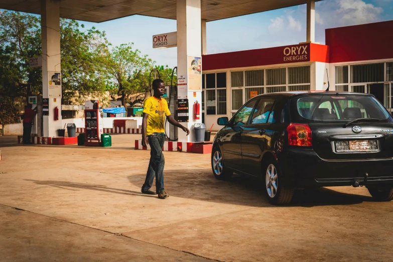 a man standing next to a car at a gas station, pexels contest winner, african sybil, square, qirex, orisha