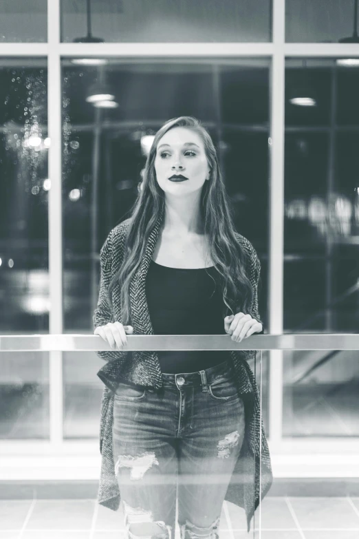 a black and white photo of a woman standing in front of a window, inspired by Elizabeth Polunin, unsplash, at a mall, portrait of maci holloway, night photo, student