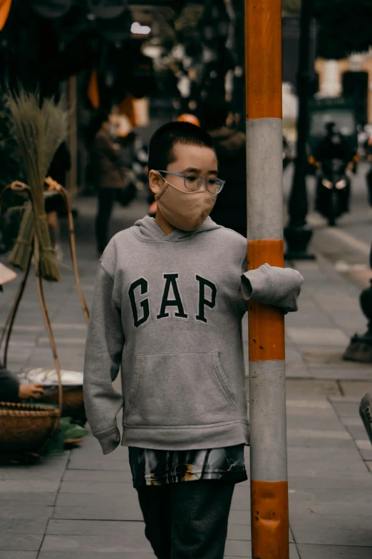 a man wearing a face mask walking down a street, an album cover, inspired by Gao Qipei, trending on unsplash, gray hoodie, little kid, poop, disappointed