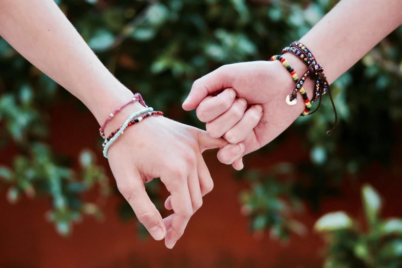 a close up of two people holding hands, an album cover, trending on pexels, bracelets, multicoloured, teenage girl, beads