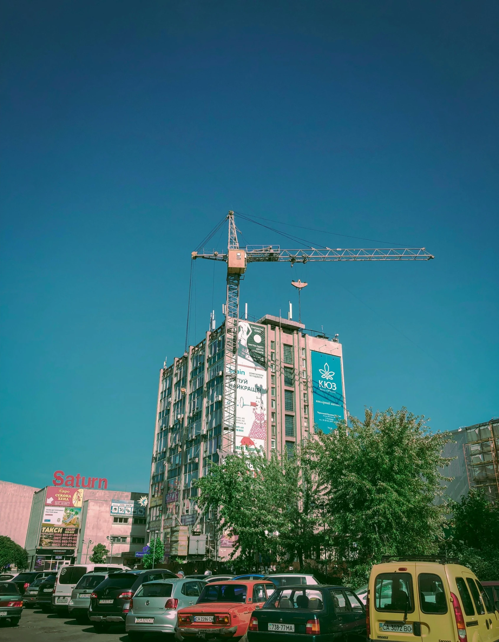 a group of cars parked in a parking lot next to a tall building, by Adam Marczyński, unsplash contest winner, constructivism, sitting in a crane, neo kyiv, billboard image, pink marble building