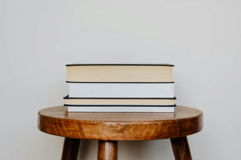 a stack of books sitting on top of a wooden table, by Carey Morris, trending on unsplash, private press, a round minimalist behind, with a white background, background image, wooden side table