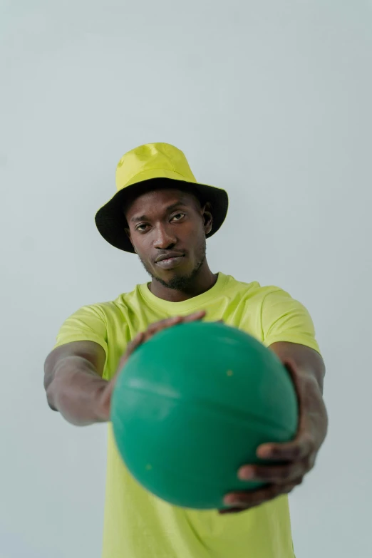 a man in a yellow shirt holding a green ball, inspired by Ernest Zobole, unsplash, he is wearing a hat, ( ( dark skin ) ), t pose, split near the left