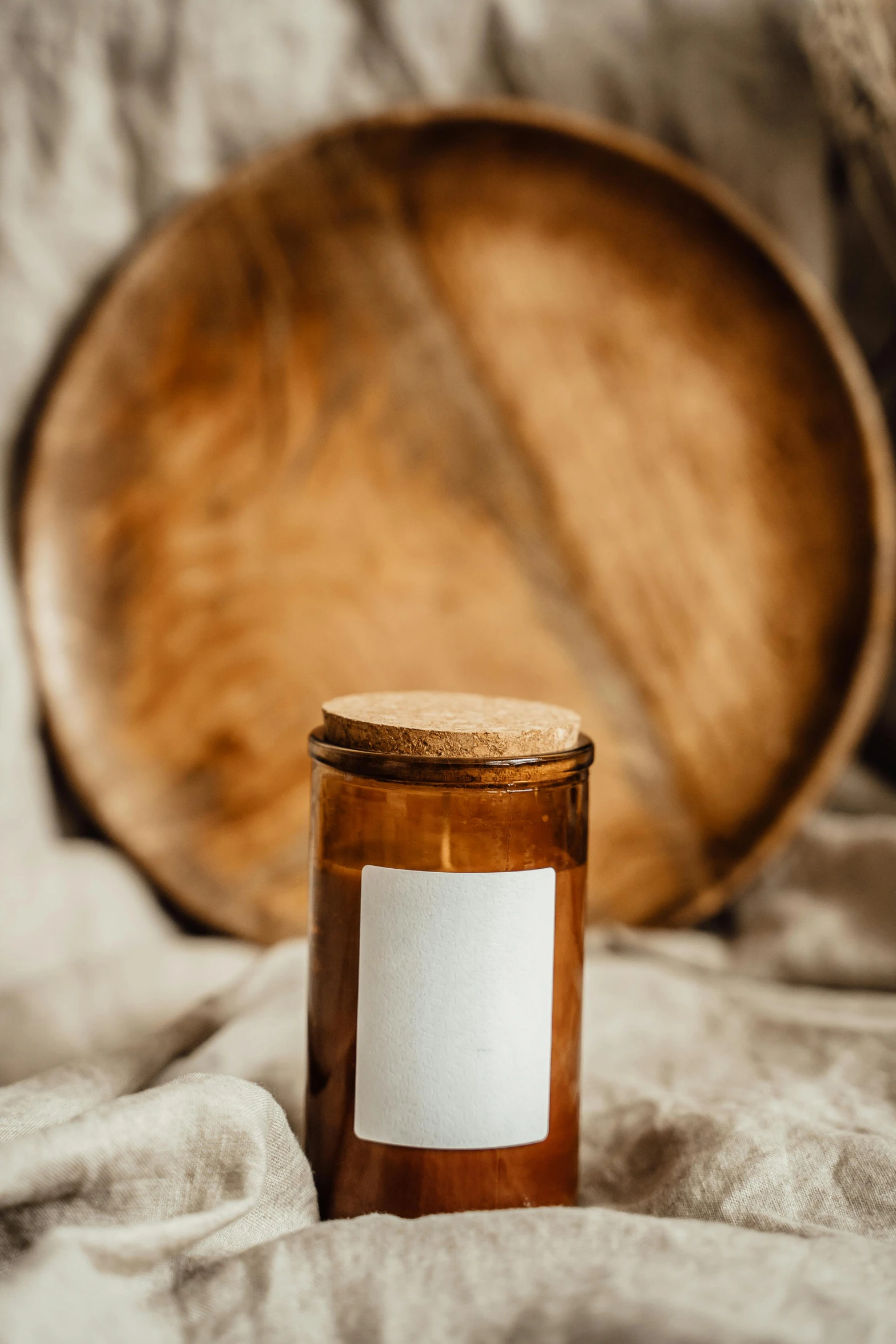 a candle sitting on top of a bed next to a wooden barrel, a picture, unsplash, label, empty background, caramel, round format