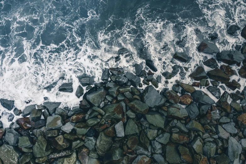 a person riding a surfboard on top of a rocky beach, an album cover, unsplash, minimalism, ((rocks)), looking down from above, charybdis, hundreds of them