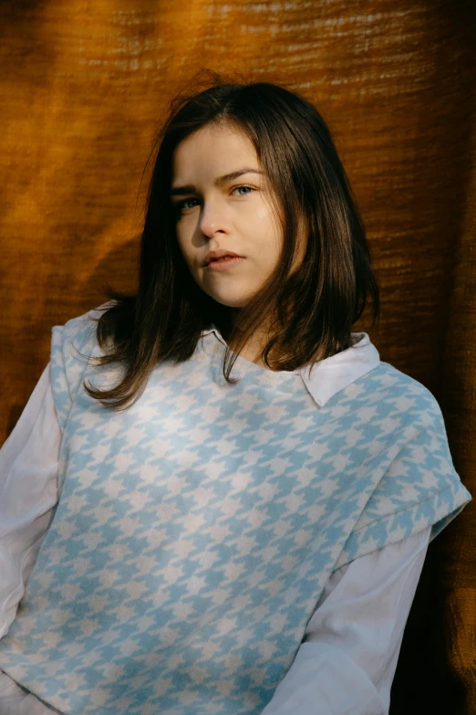 a woman sitting on a chair in front of a curtain, an album cover, inspired by Louisa Matthíasdóttir, trending on unsplash, private press, wearing a light blue shirt, flannel, frown fashion model, patterned clothing