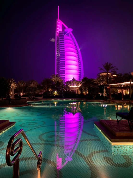 a swimming pool at night with the burjra in the background, fuschia leds, front shot, exterior