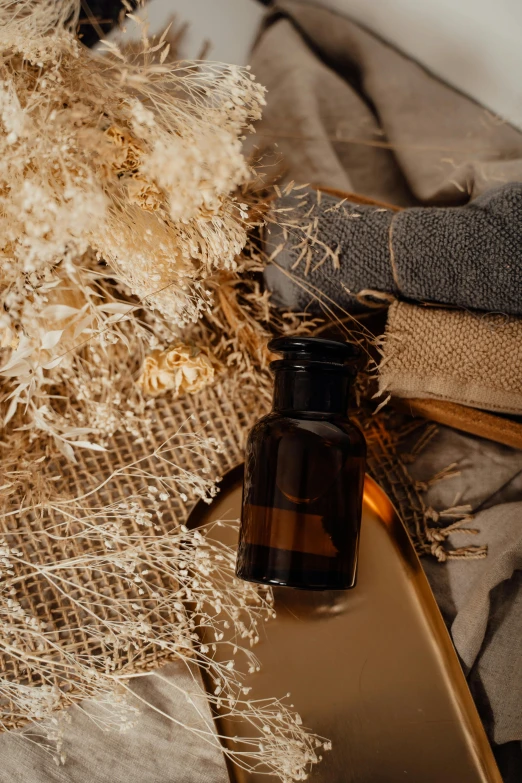 a bottle of essential oil sitting on top of a bed, by Andries Stock, trending on pexels, renaissance, made of dried flowers, brown and gold, cloth accessories, hay