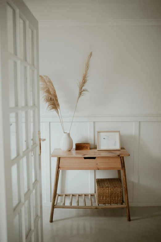 a white vase sitting on top of a wooden table, in a white room, willowy frame, exiting from a wardrobe, in a white boho style studio