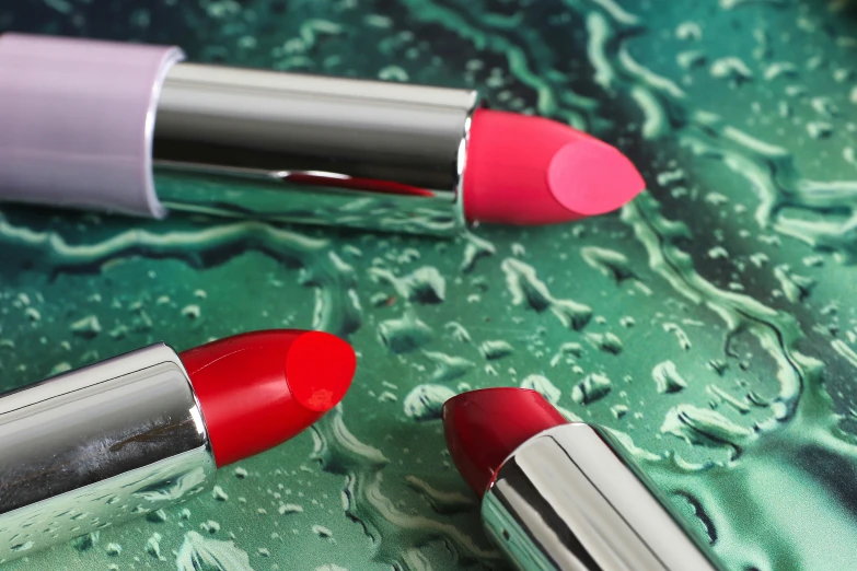 a couple of lipsticks sitting on top of a table, shutterstock contest winner, photorealism, silver red, vibrant bright colours, view from bottom to top, artdeco