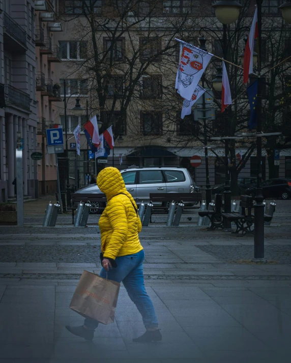 a person in a yellow jacket walking down a street, by Grytė Pintukaitė, pexels contest winner, socialist realism, lgbt, wet climate, polish hyper - casual, carrying big sack