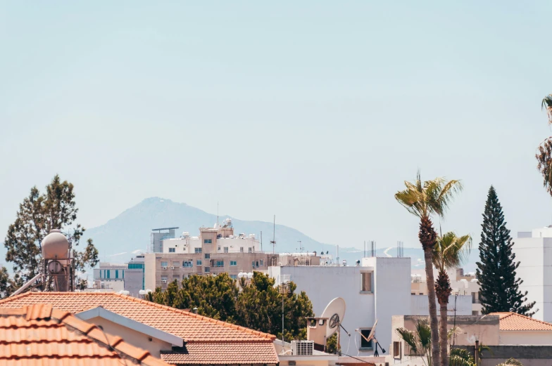 a view of a city with palm trees in the foreground, by Daniel Lieske, trending on unsplash, cyprus, background image, roof with vegetation, with a volcano in the background