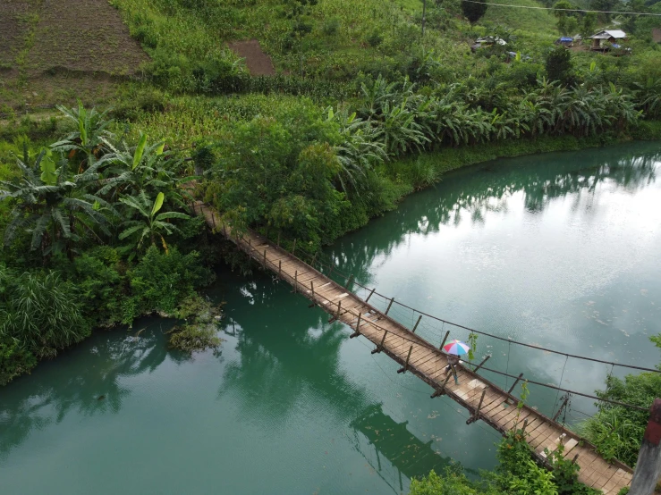 a man walking across a suspension bridge over a river, hurufiyya, blue and green water, shipibo, slide show, small lake