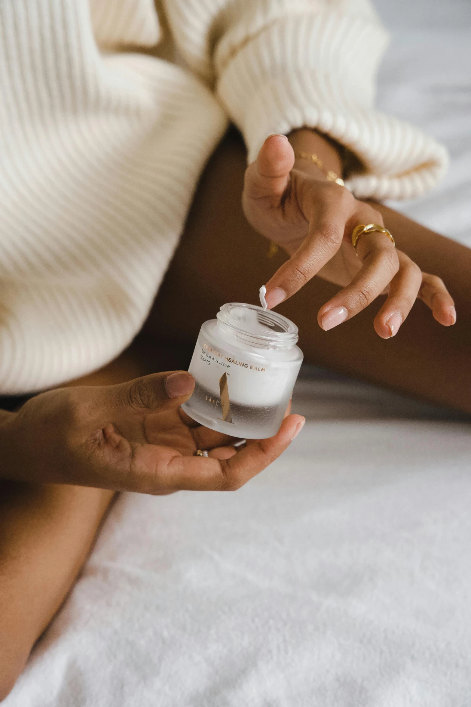 a woman sitting on a bed holding a jar of cream, by Nina Hamnett, trending on pexels, renaissance, detailed white, silicone skin, glass jar, angled