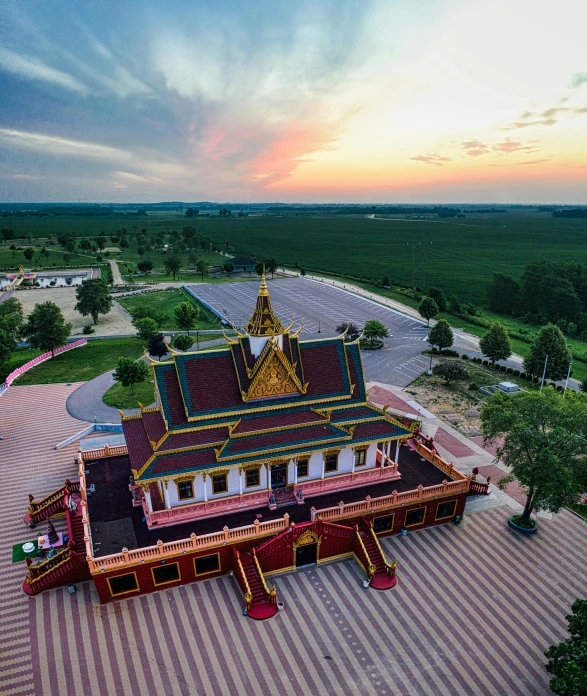 a large building sitting on top of a lush green field, by Matthias Stom, unsplash contest winner, cambodia, russian temple, drone wide shot, sundown