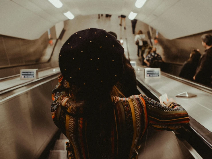 a woman standing on an escalator with her back to the camera, by Emma Andijewska, pexels contest winner, afrofuturism, paisley, fully dressed, underground scene, covered in jewels