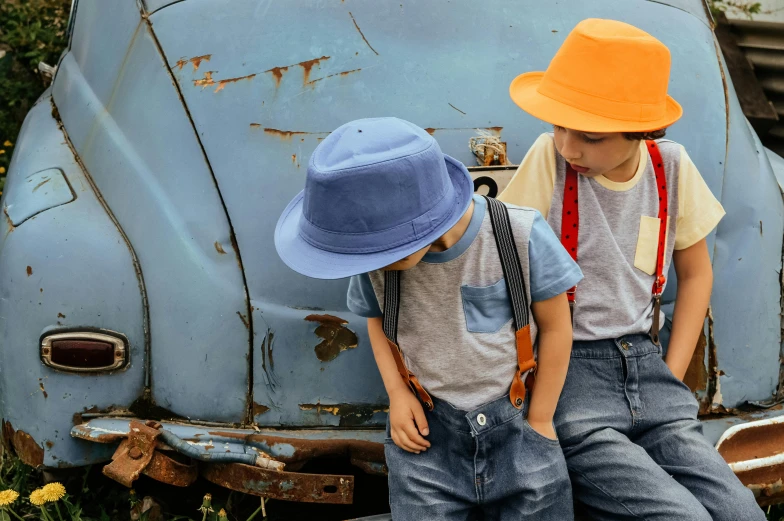 two young boys sitting on the back of a blue car, pexels, bucket hat, coloured in blueberra and orange, suspenders, wearing a fedora