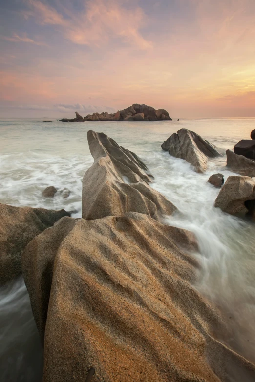 a group of rocks sitting on top of a sandy beach, by Patrick Ching, malaysian, waves crashing at rocks, granite, sunset