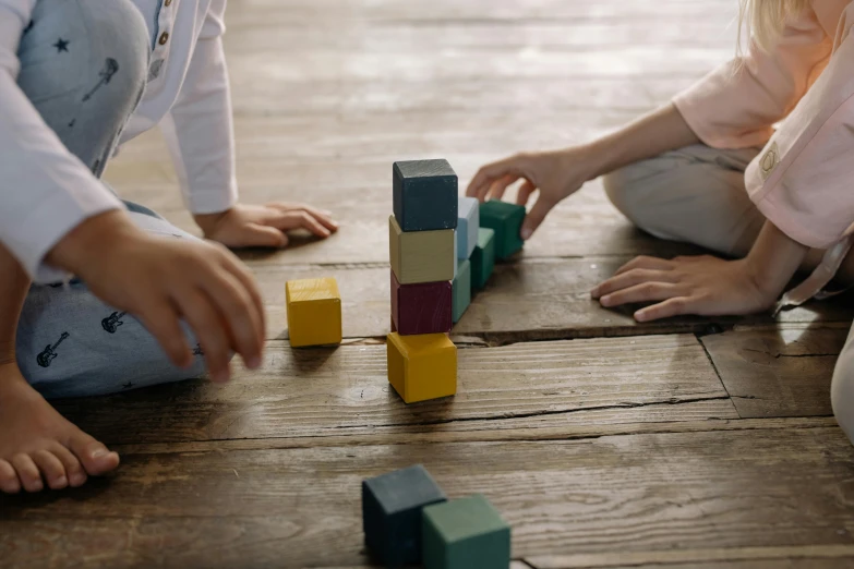 two children playing with wooden blocks on the floor, by Sebastian Vrancx, pexels contest winner, towering above a small person, on a wooden table, zoomed in, square shapes