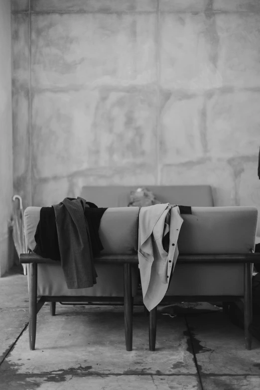 a black and white photo of a person sitting on a couch, by Caro Niederer, minimalism, tattered cloth robes, behind the scenes, still from l'estate, tailored clothing