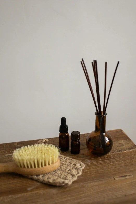 a wooden table topped with a brush and a bottle of essential oils, by Ruth Simpson, spa, tiny sticks, deco, brown:-2
