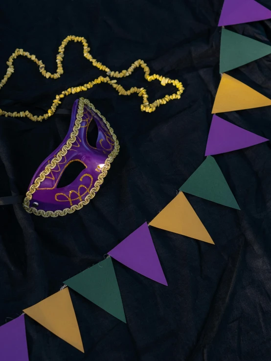 a purple mask sitting on top of a black cloth, an album cover, trending on unsplash, renaissance, red pennants, green and gold, ((purple)), may)