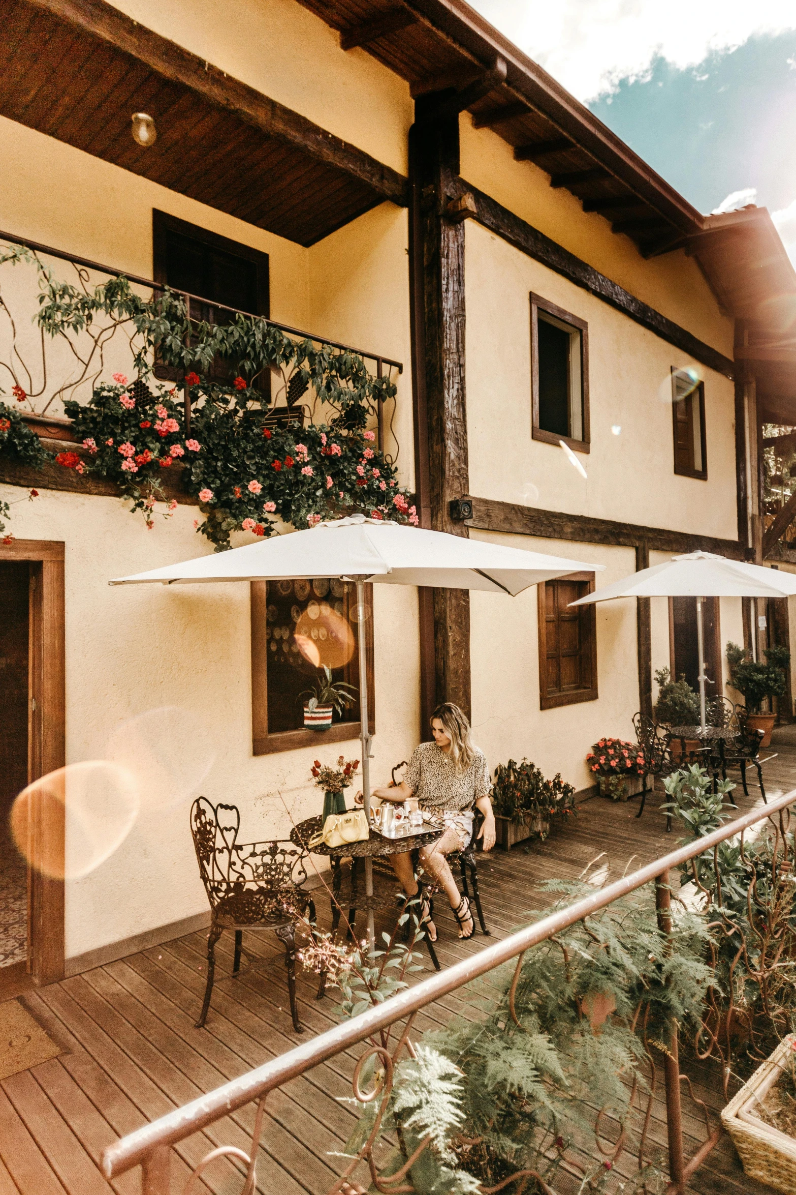 a patio area with tables, chairs and umbrellas, a portrait, by Julia Pishtar, pexels contest winner, art nouveau, chalet, brazil, sitting with flowers, woman drinking coffee