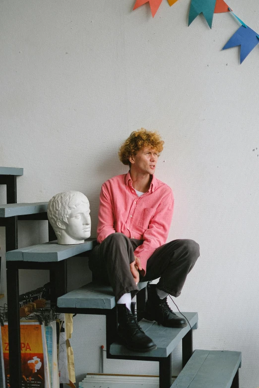 a man sitting on top of a set of stairs, an album cover, by Lasar Segall, unsplash, renaissance, sophia lillis, curly pink hair, sculptor, in a studio