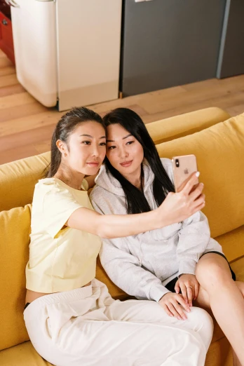 two women sitting on a couch taking a selfie, a picture, inspired by Wang Duo, trending on pexels, realism, asian male, yellow hue, teenagers, professional iphone photo
