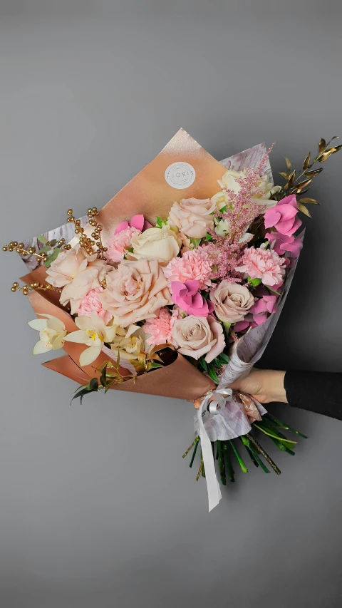 a person holding a bouquet of pink and white flowers, on grey background, pink and gold color scheme