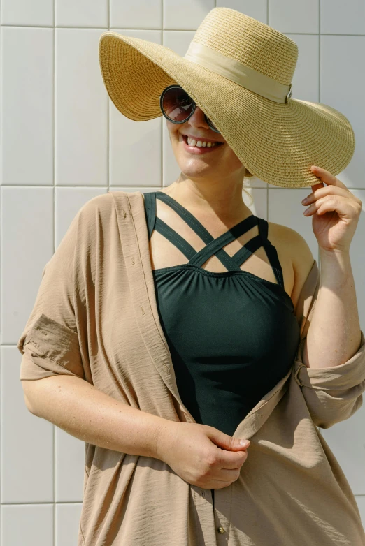 a woman standing in front of a wall wearing a hat, green swimsuit, open jacket, wearing : tanktop, modern earthy neutral earthy