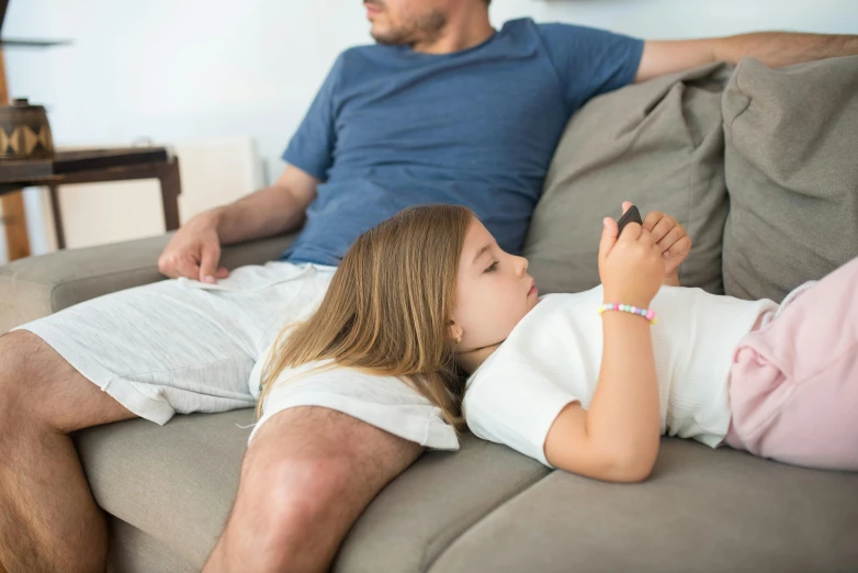 a man and a little girl laying on a couch, pexels, looking at his phone, tv still, sleek hands, aged 13