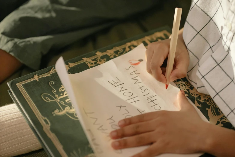 a person holding a pencil and writing on a piece of paper, by Emma Andijewska, with some hand written letters, decoration, green letters, thumbnail