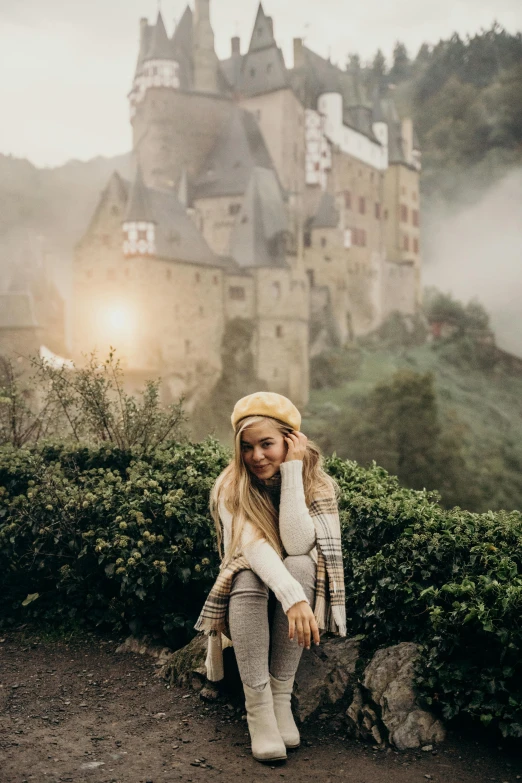 a woman sitting on a rock in front of a castle, pexels contest winner, wearing beanie, 🍂 cute, germany, dreamy hazy