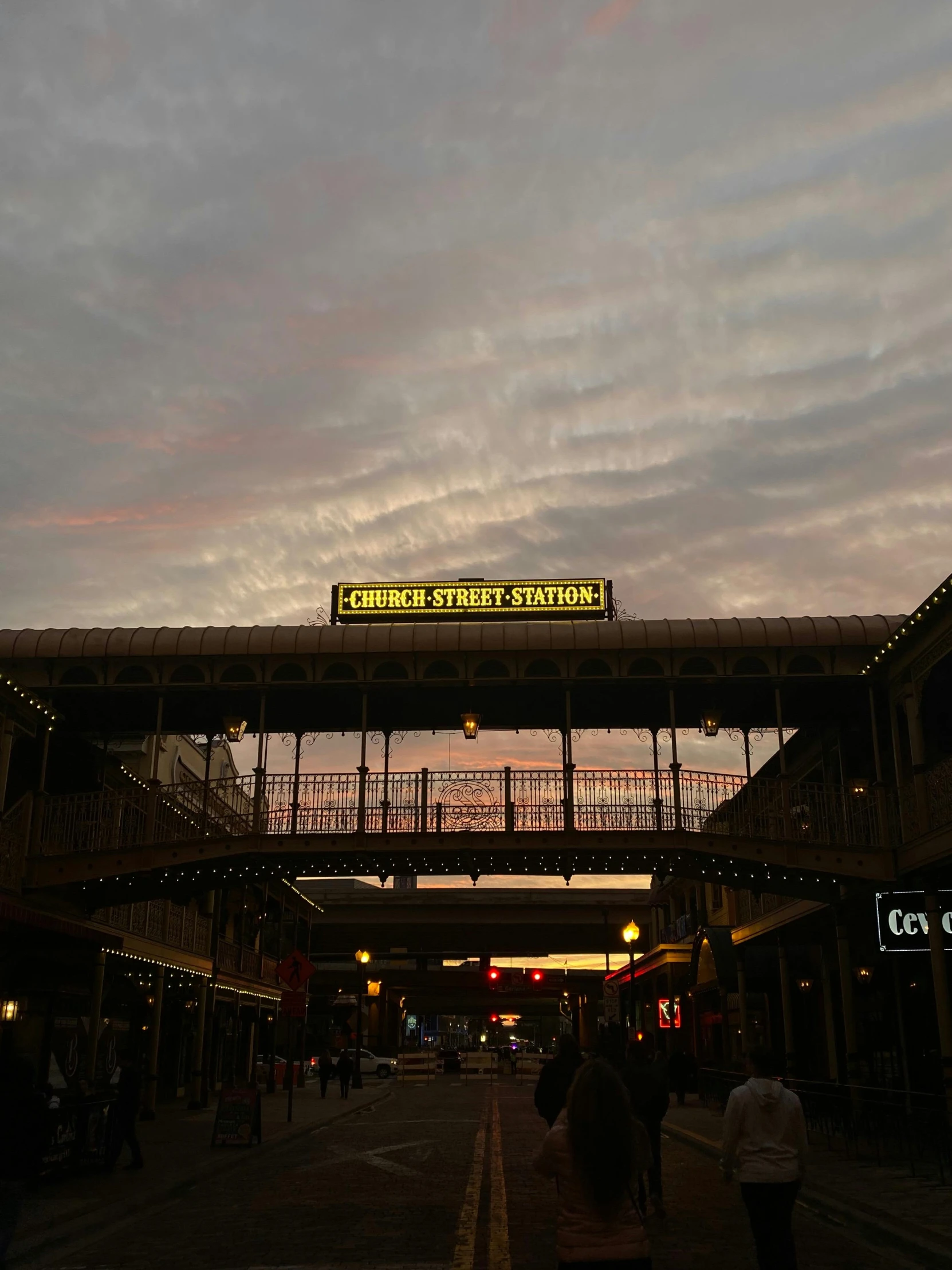 a couple of people walking down a street under a bridge, in the evening, station, sign, there are archways