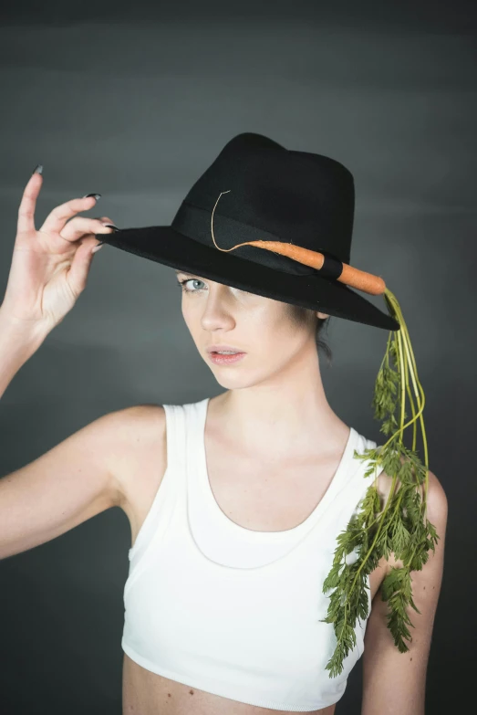 a woman in a hat holding a bunch of carrots, an album cover, inspired by Josefina Tanganelli Plana, unsplash, black fedora, non binary model, anna nikonova aka newmilky, personification of marijuana