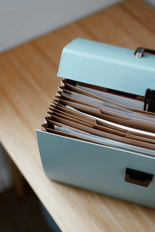 a blue briefcase sitting on top of a wooden table, by Jessie Algie, unsplash, happening, scientific document, pastel hues, open vault, collection product