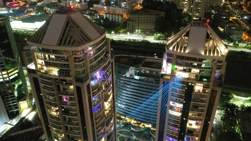 an aerial view of a city at night, a hologram, holography, singapore esplanade, back lit vertigo fear of heights, lasers for lights, raising between the buildings